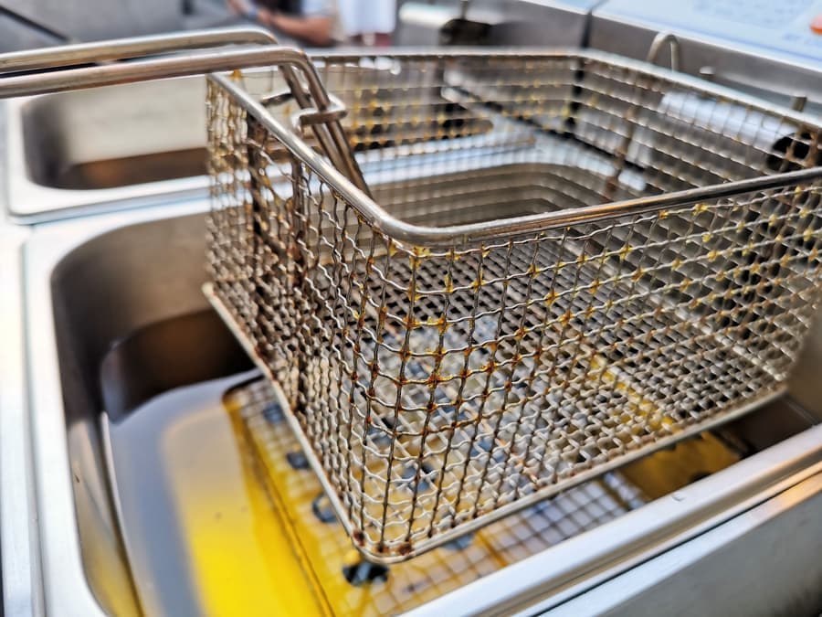 A metal frying basket lifted out of a deep fryer